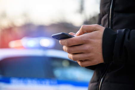 man holding phone with police car in street