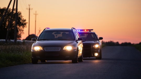 Speeding Driver Gets Pulled Over By Police Patrolling Car . Wide Shot of the Two Cars Stopped in a Road Crossing an Open Field. Drunk Driver Gets Caught by Professional Officers