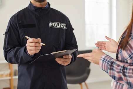 Policeman interrogating woman or witness regarding police investigation. Male police officer in uniform writing down testimonies to investigate burglary. Police investigation concept